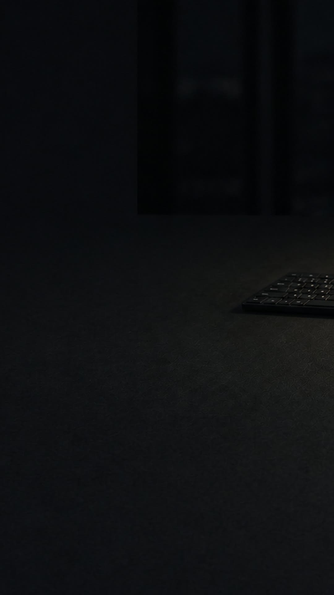 A dim night operations desk: a small device with one green status light and a notebook on a dark table, a dark city skyline in the window.